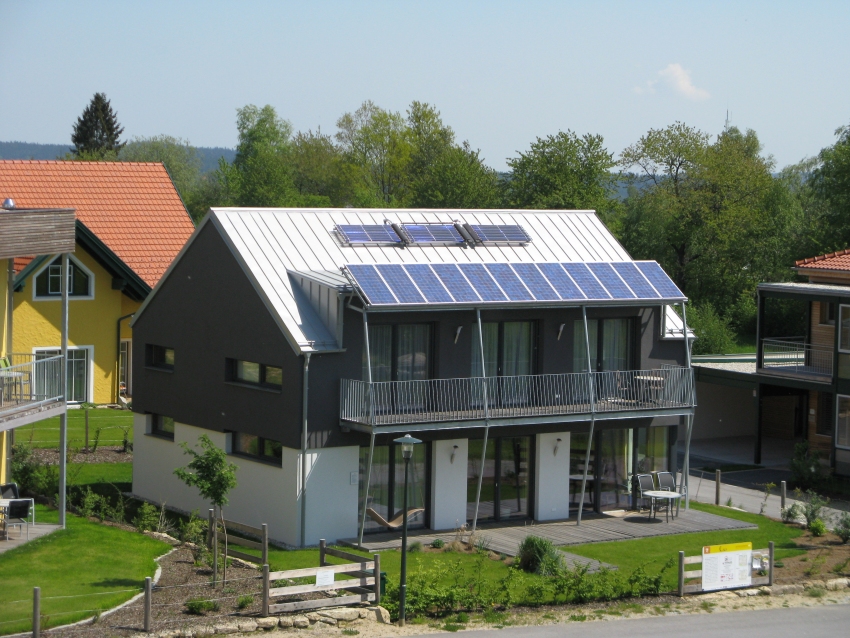 Dunkles Haus mit weißem Erdgeschoss und großen Photovoltaik-Modulen auf dem Satteldach.