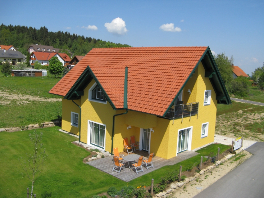 Gelbes Einfamilienhaus mit Satteldach und Balkon in Passivhaus-Bauweise.