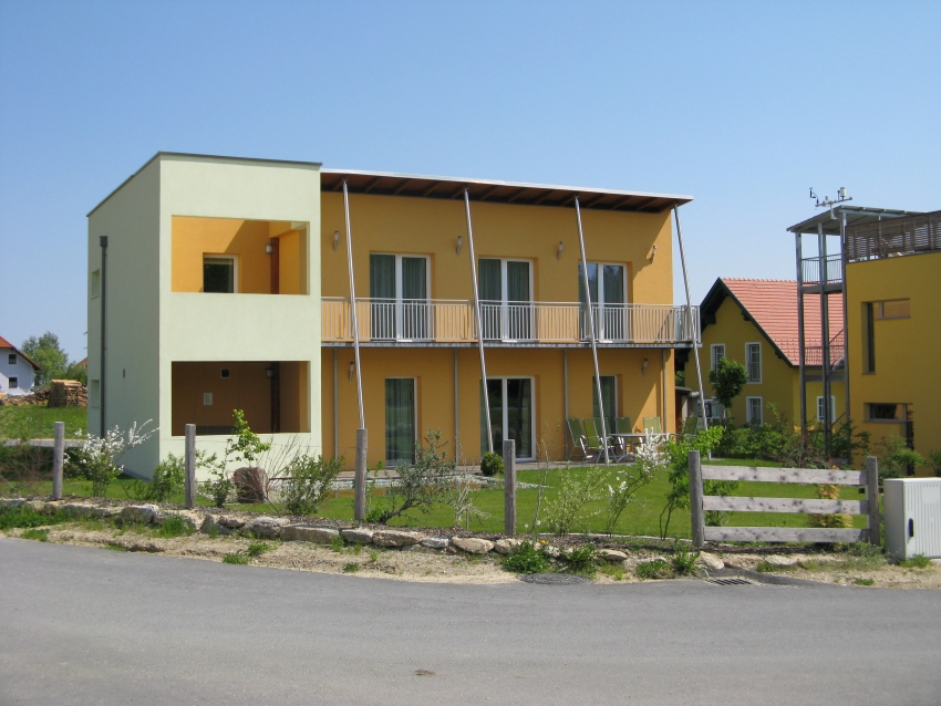 Modernes, gelbes Gebäude mit Pultdach und markanten Stützen vor der Fassade.